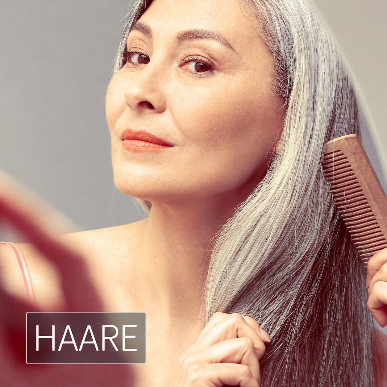 Ältere Frau mit langen grauen Haaren kämmt ihr Haar mit einem Holzkamm. Text: Haare.