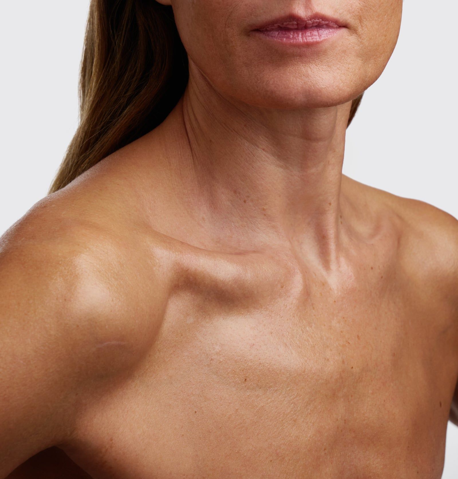 Nahaufnahme von Hals und Schultern einer Person. Hautton: hellbraun. Beleuchtung betont die Hautstruktur.