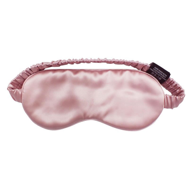 Rosa Schlafmaske aus Seide mit elastischem Band. Schwarzes Etikett mit Pflegehinweisen.