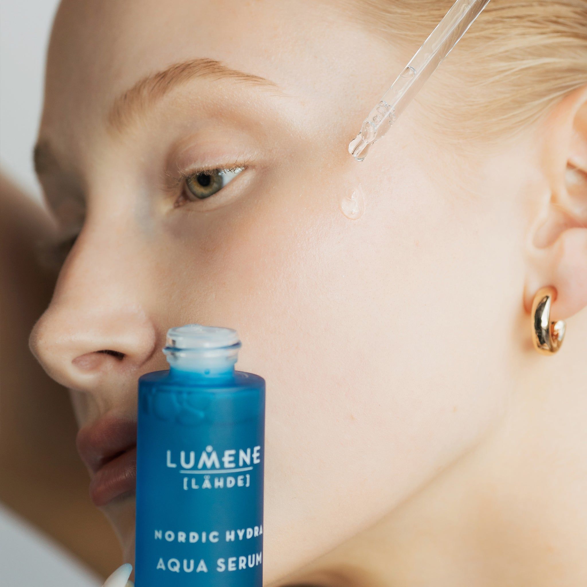 Frau mit Serumflasche und Pipette. Serum wird auf die Haut aufgetragen. Aufschrift: Lumene [LAHDE] Nordic Hydra Aqua Serum.