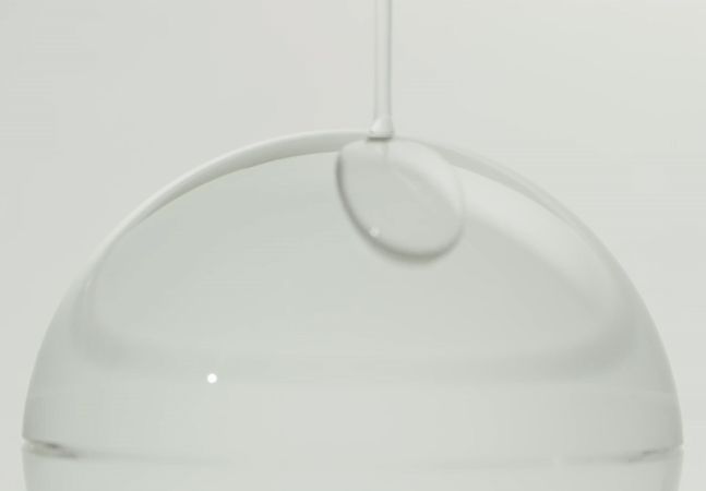 Tropfen AYUNCHE Derma Calming Scalp Serum auf einer Oberfläche.