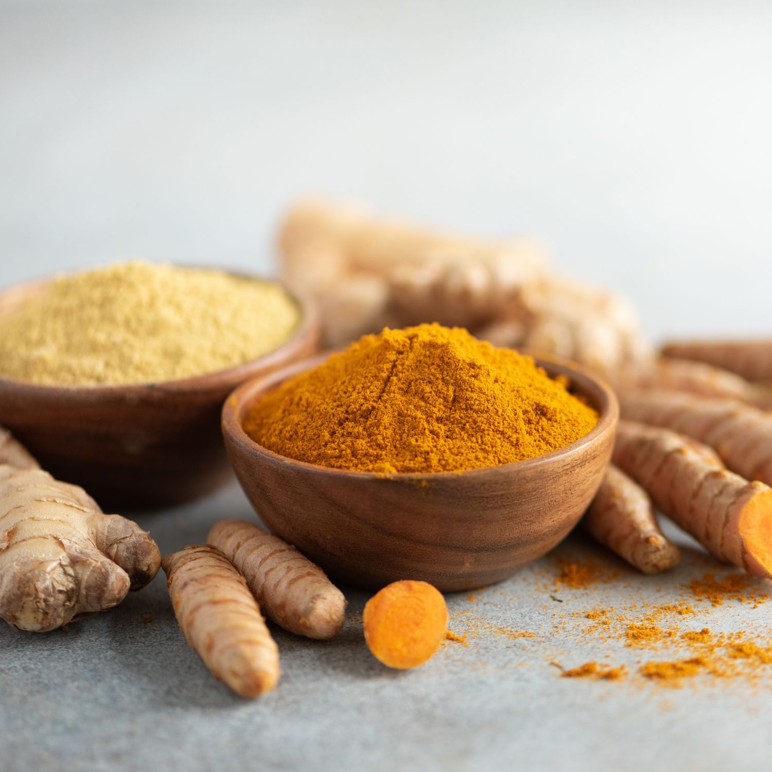 Holzschalen mit Kurkuma- und Ingwerpulver. Frischer Ingwer und Kurkuma-Wurzeln daneben.
