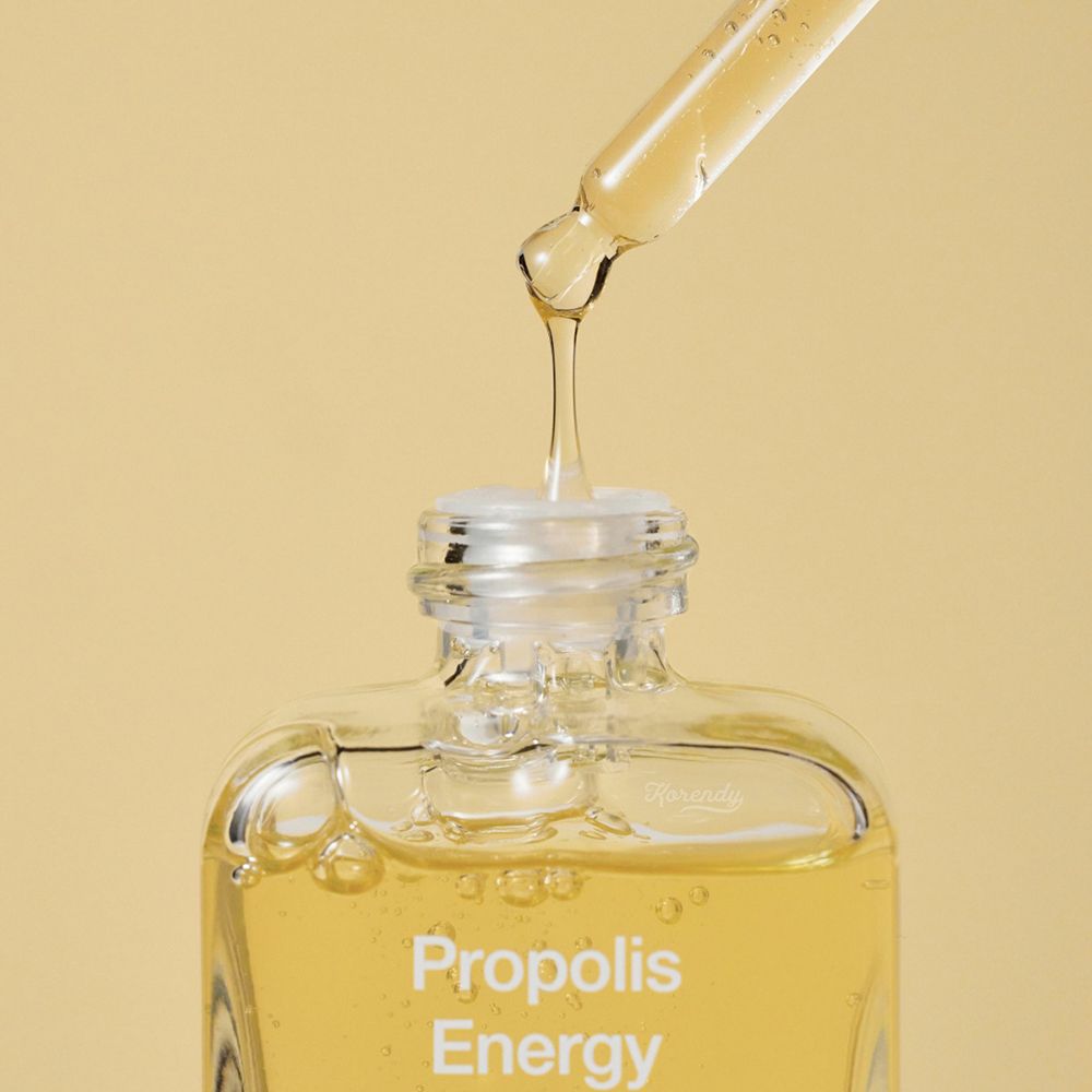 Nahaufnahme einer Flasche mit gelber Flüssigkeit. Pipette tropft Flüssigkeit. Aufschrift: Propolis Energy.