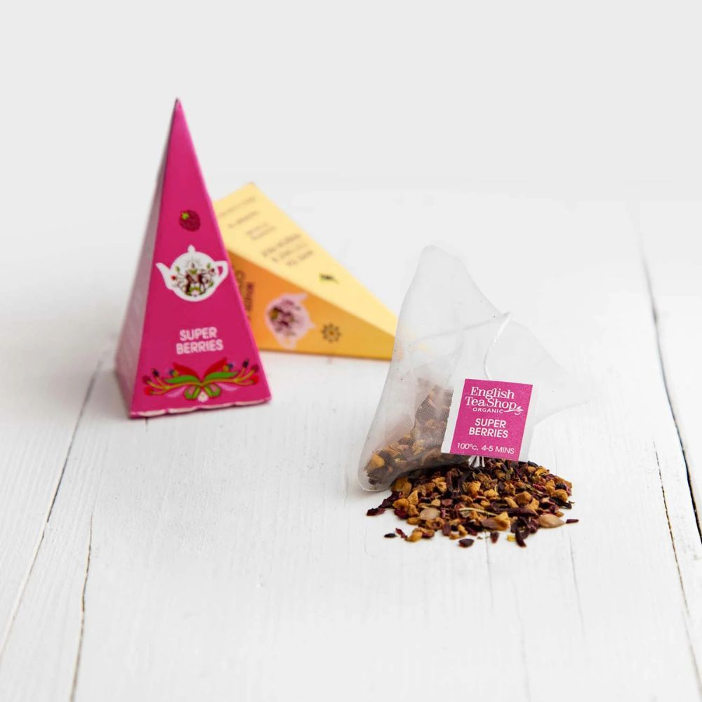 Rosa und gelbe Pyramidenboxen mit Teebeutel und losem Tee. Aufschrift: Super Berries. Teebeutel mit Aufschrift Super Berries.