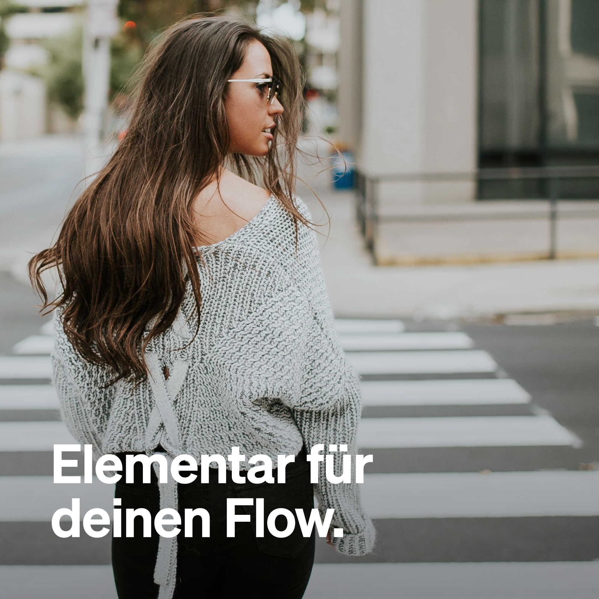 Eine Frau überquert einen Zebrastreifen. Sie trägt eine Brille und einen grauen Pullover. Text: Elementar für deinen Flow.