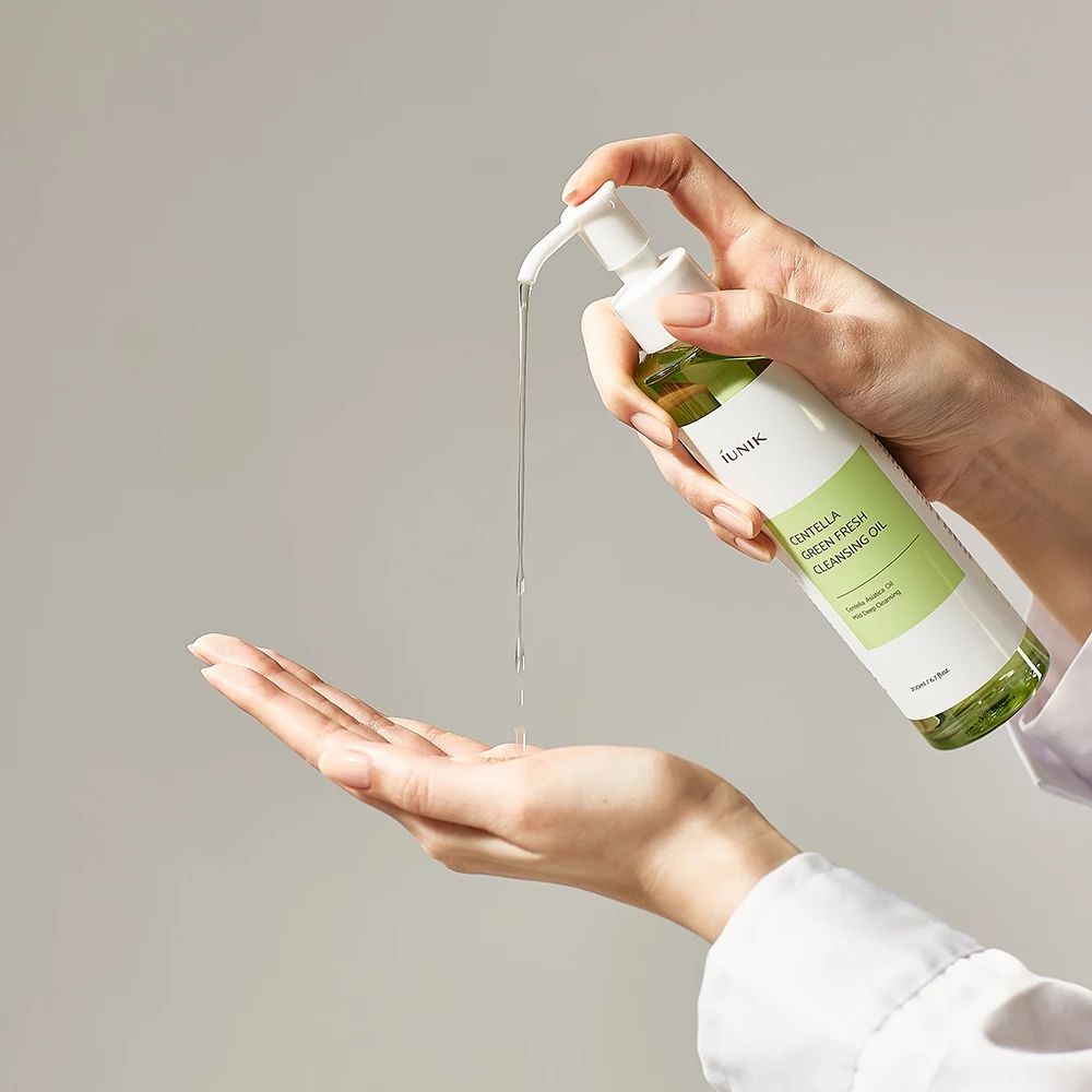 Hände halten eine Flasche, Öl wird abgegeben. Aufschrift: iUNIK Centella Green Fresh Cleansing Oil.