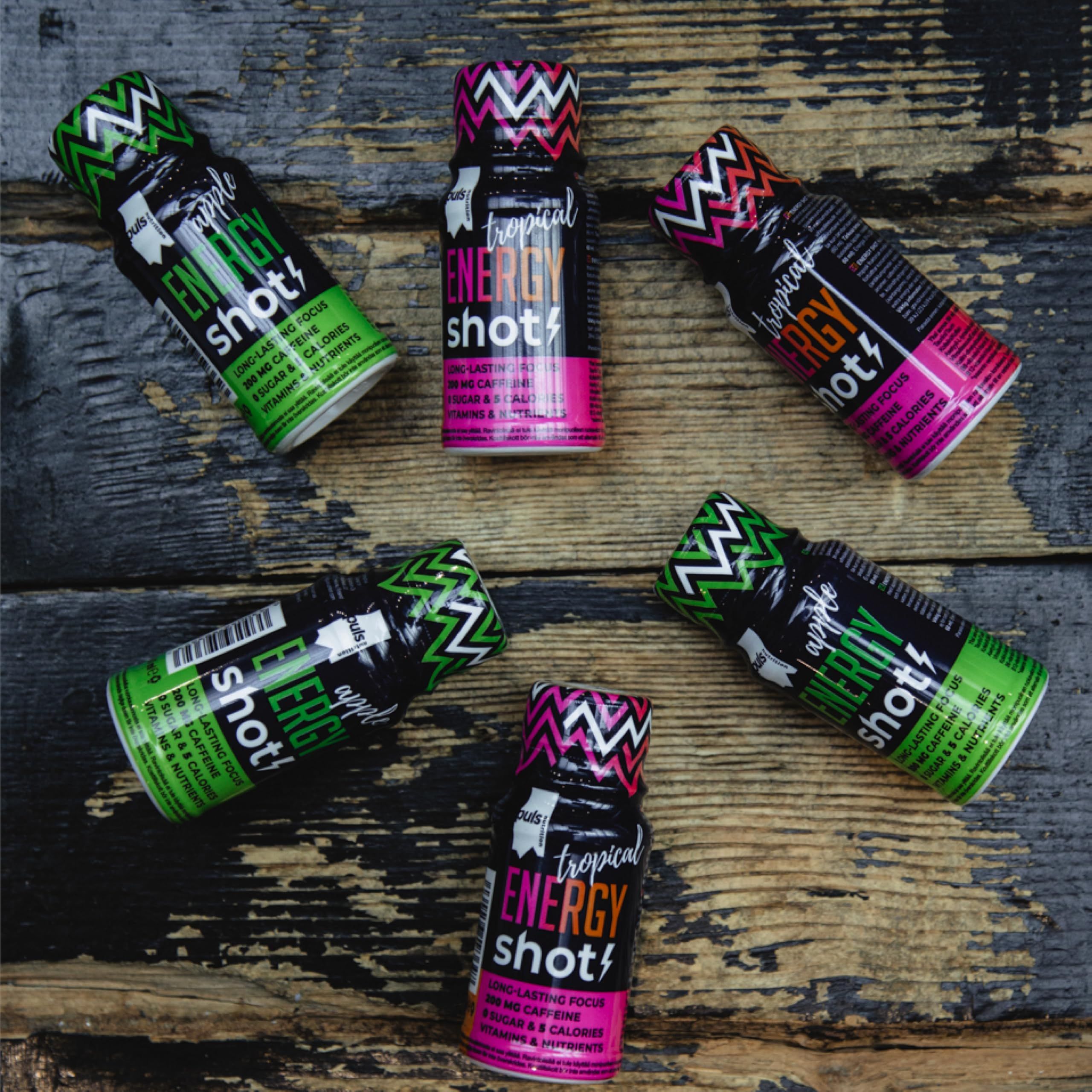 Fünf Puls Nutrition Energie Shots Apfel und zwei Tropical Energy Shots auf Holzhintergrund.