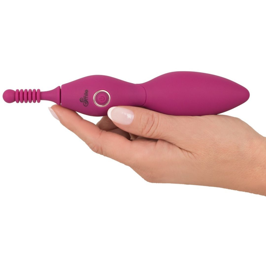Pinkfarbener Vibrator in einer Hand gehalten. Der Vibrator hat eine längliche Form mit einem Knopf und einem geriffelten Ende.