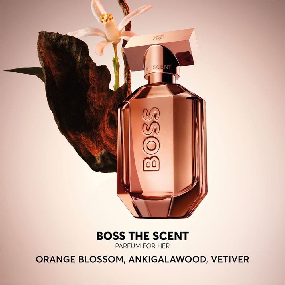 Hugo Boss The Scent Eau de Parfum Flakon neben einem Stück Holz und einer Blüte.