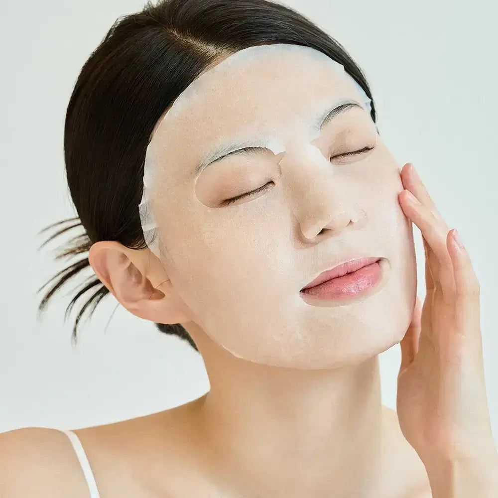 Gesicht einer Frau mit einer Gesichtsmaske. Die Maske bedeckt die Haut. Eine Hand berührt die Wange.