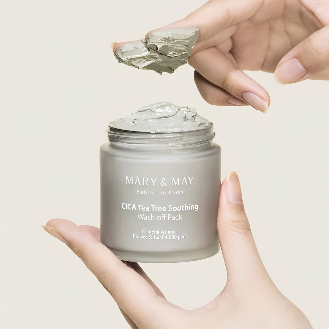 Hände nehmen eine kleine Menge der grauen Mary & May CICA Tea Tree Soothing Wash off Pack aus dem Behälter.