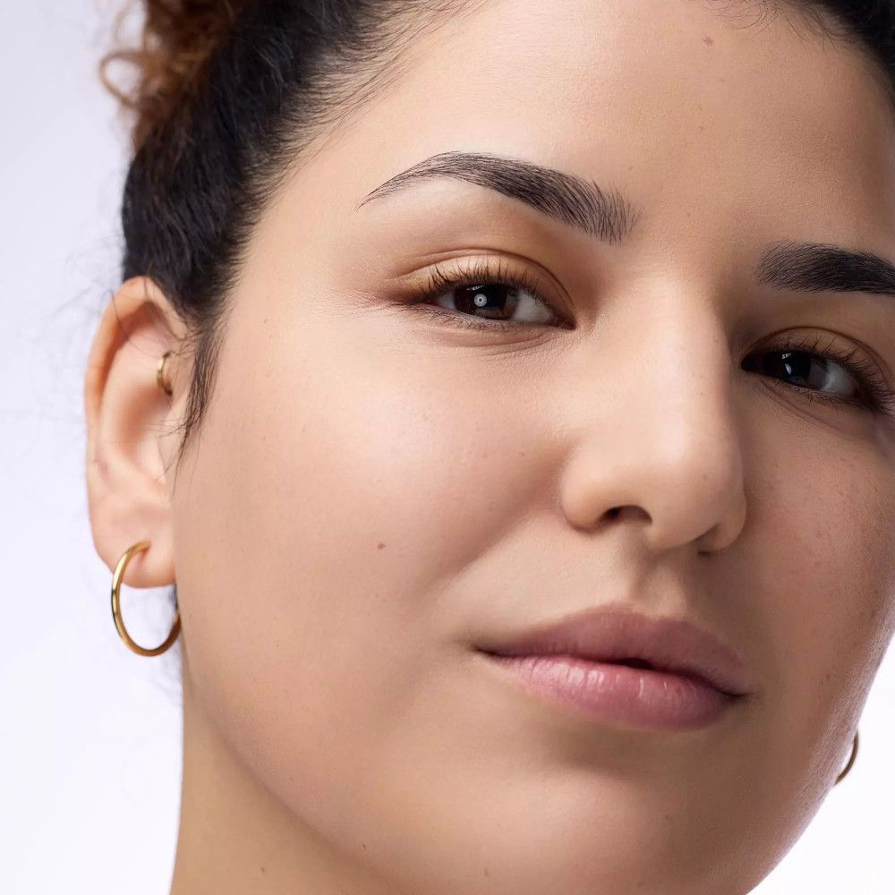 Nahaufnahme einer Frau mit geschminktem Gesicht. Sie trägt goldene Creolen.