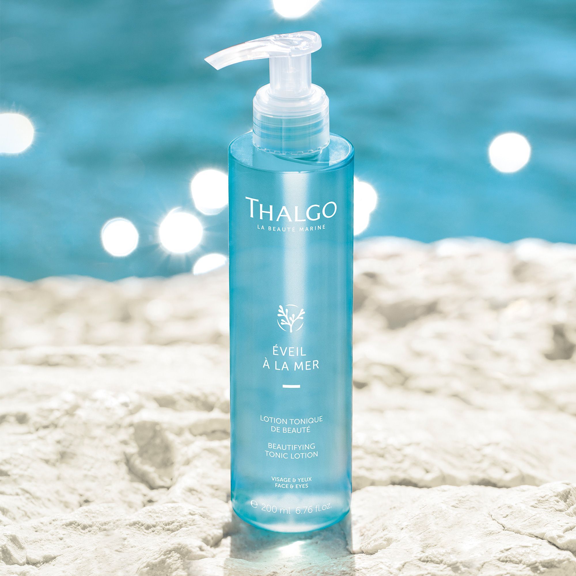 Blau-transparente Flasche mit Pumpe, auf Stein vor Wasser. Aufschrift: THALGO, ÉVEIL À LA MER, Lotion Tonique de Beauté.