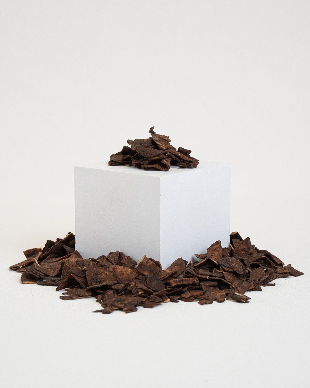 Haufen von Kokoschips mit Kakao auf einem weißen Podest, umgeben von weiteren Chips.