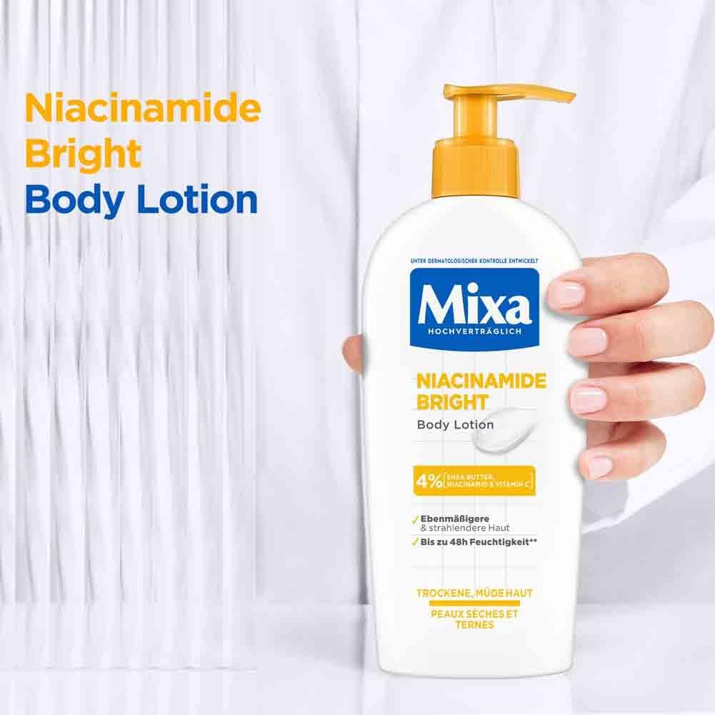 Eine Hand hält eine Flasche Mixa Niacinamide Bright Body Lotion. Aufschrift: Niacinamide Bright Body Lotion. Enthält 4% Niacinamide.