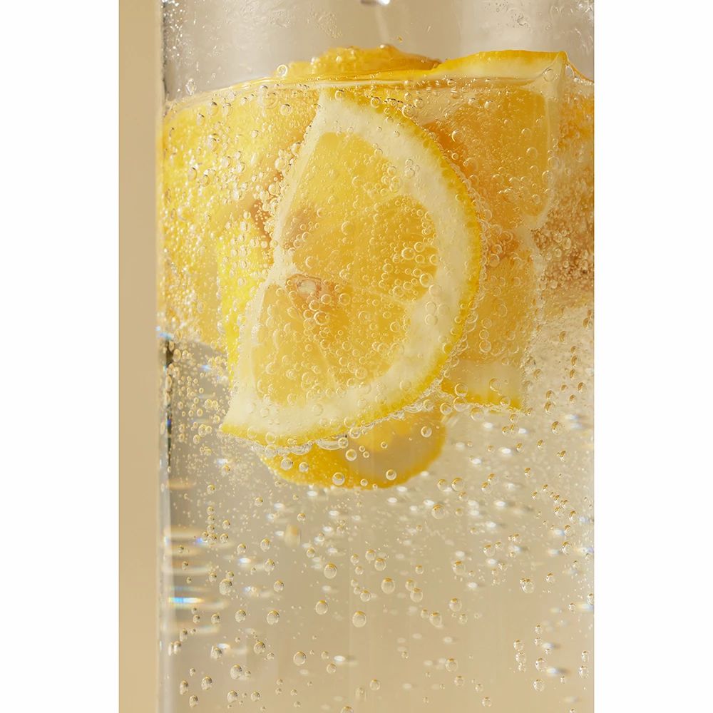 Glas mit Zitronenscheiben und Blasen. Flüssigkeit ist gelblich.