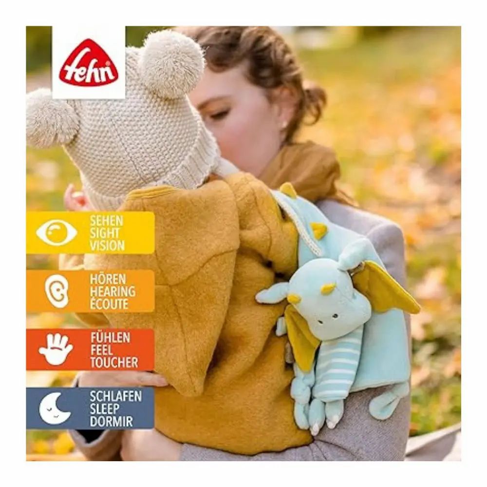 Baby mit Stoffdrachen im Arm. Marke: Fehn. Symbole für Sehen, Hören, Fühlen, Schlafen. Gelbe Jacke.