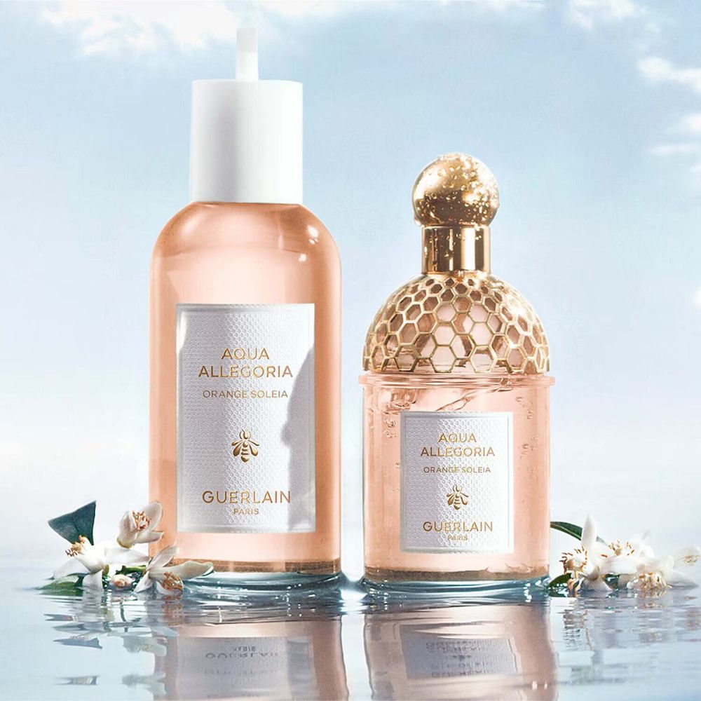 Zwei Parfumflakons neben Blüten. Flakons mit Aqua Allegoria, Orange Soleia und Guerlain-Etiketten. Hintergrund: Wasser.