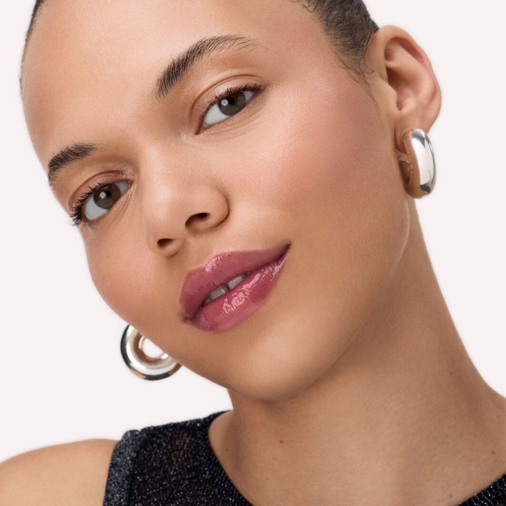 Porträt einer Frau mit aufgetragenem Catrice Peptide Bliss Glossy Lip Balm. Glänzende Lippen, silberne Ohrringe.