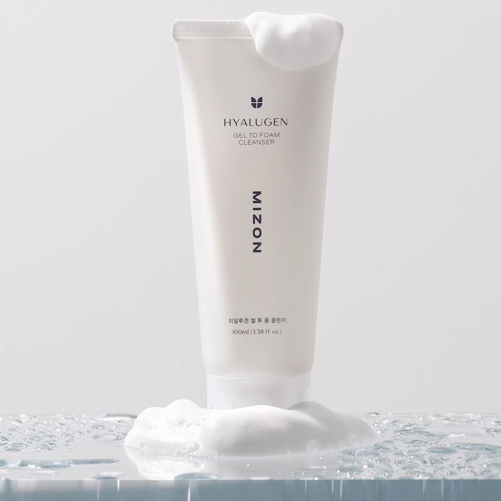 Weiße Tube mit Produkt und Schaum. Aufschrift HYALUGEN, GEL TO FOAM CLEANSER, MIZON. Schaum um die Tube.