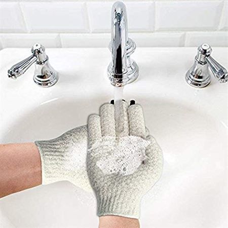 Hände mit Seifenschaum unter einem Wasserhahn, tragen hellgraue Peeling-Badehandschuhe.