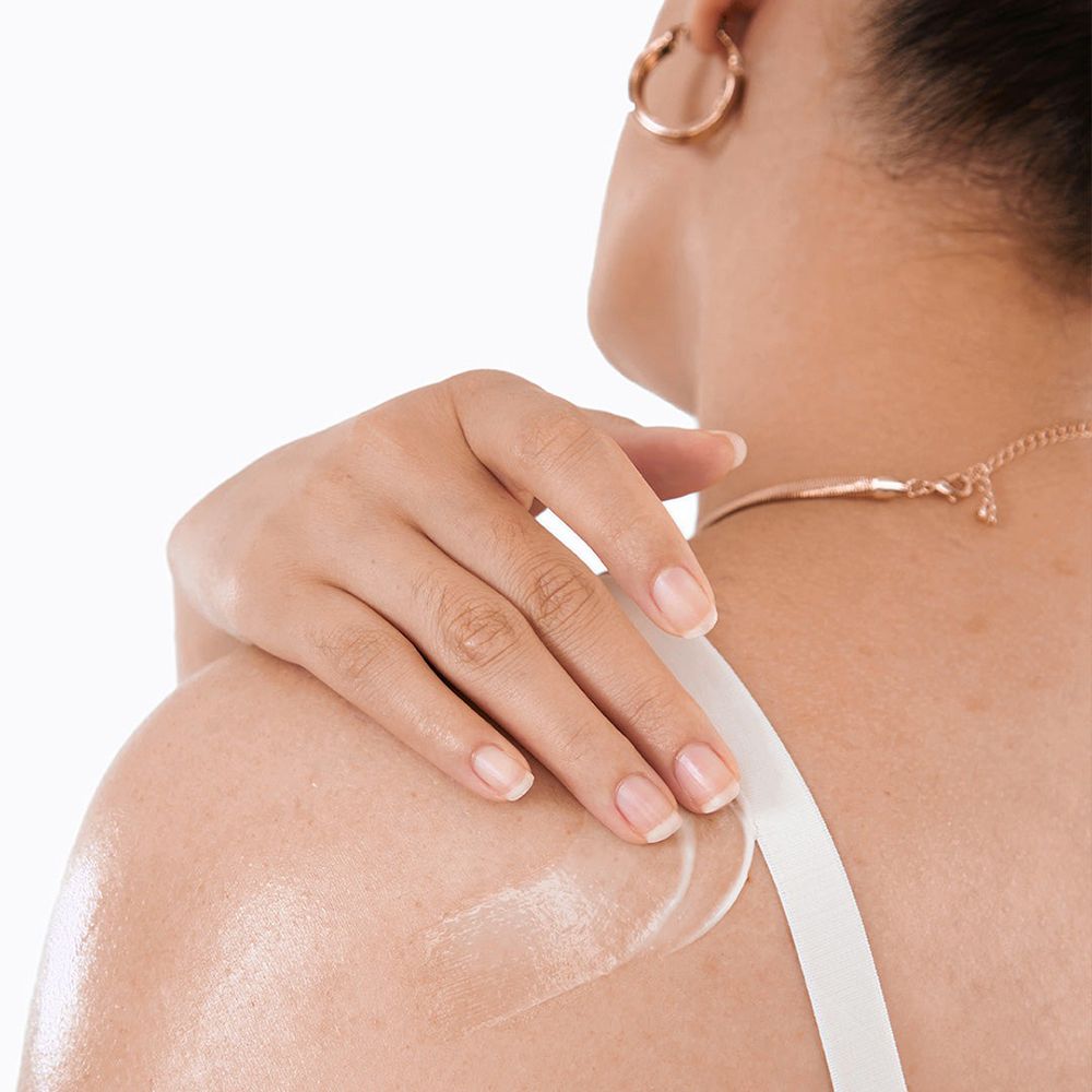 Person mit Lotion auf Schulter. Lotion auf Haut aufgetragen. Weißes Top. Goldene Halskette und Ohrring.