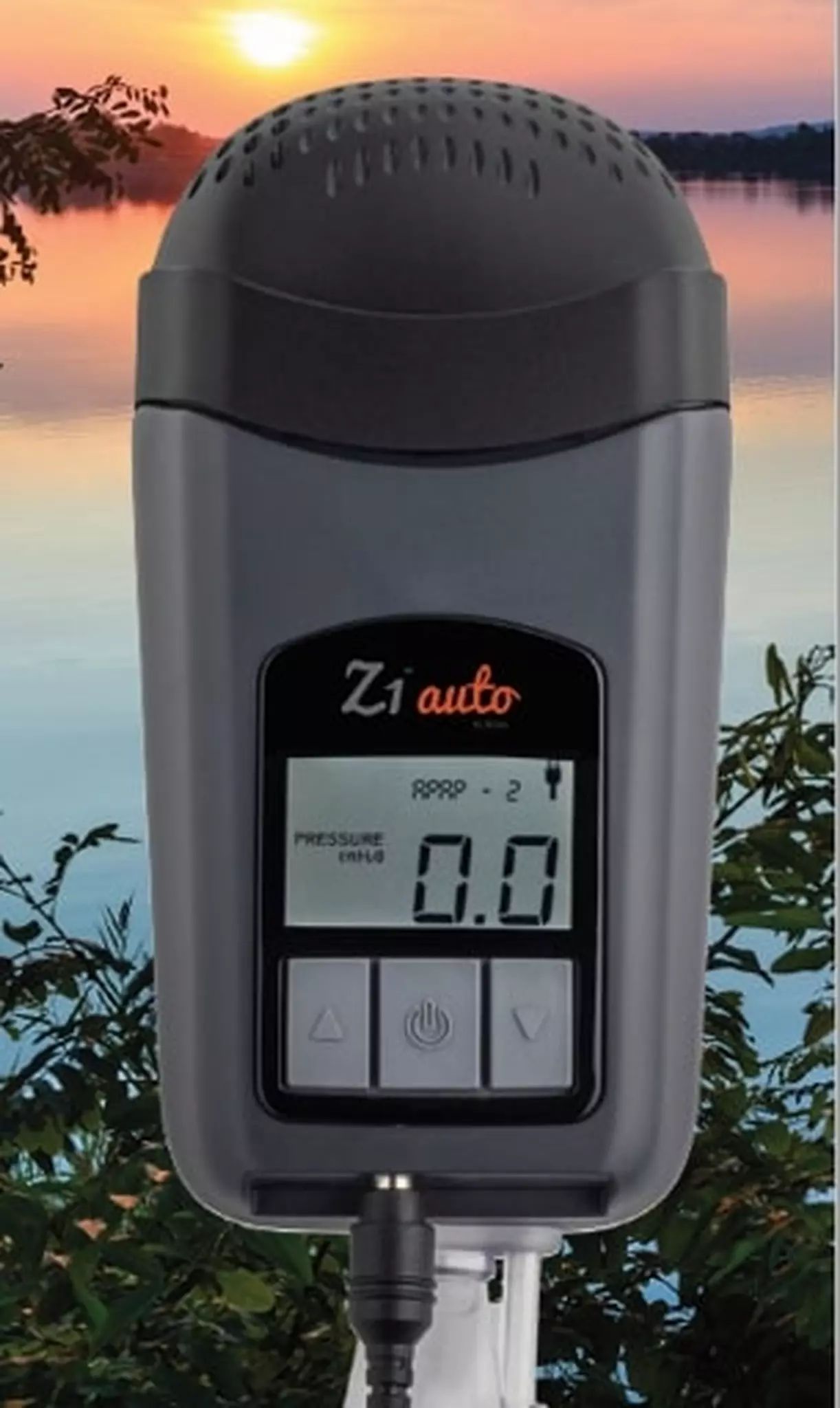 Graues Reise-CPAP-Gerät mit Display, zeigt "0.0", vor See und Bäumen.
