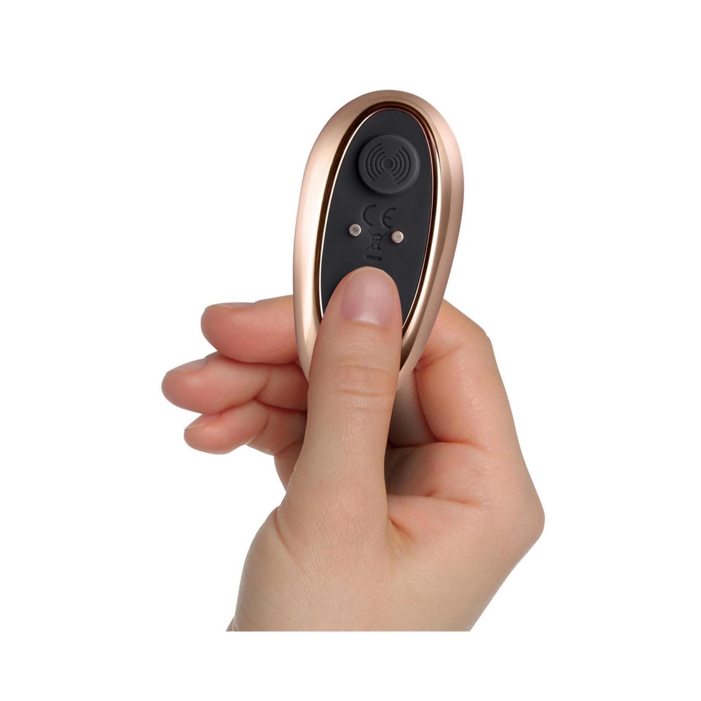 Hand hält goldfarbene Fernbedienung. Fernbedienung mit lila Knöpfen. Zwei Knöpfe mit Symbolen.