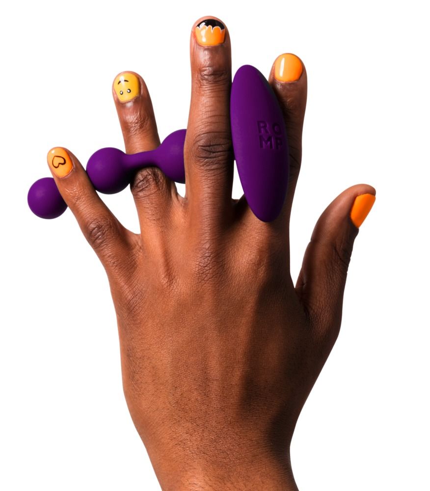 Lila Analperlen und ein Vibrator, gehalten von einer Hand. Gelbe und orangefarbene Nagelkunst.