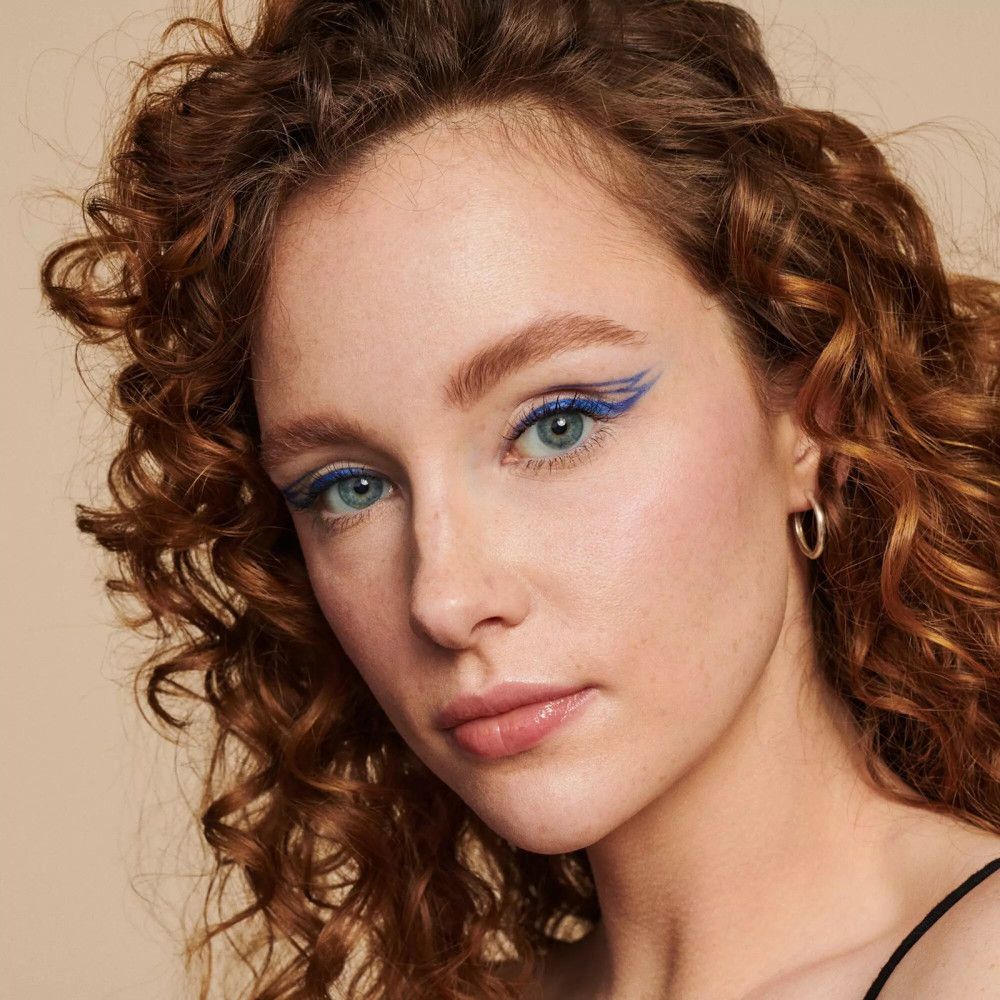 Porträt einer Frau mit blauer Eyeliner. Lockiges Haar, silberne Creolen. Hautton: hell.