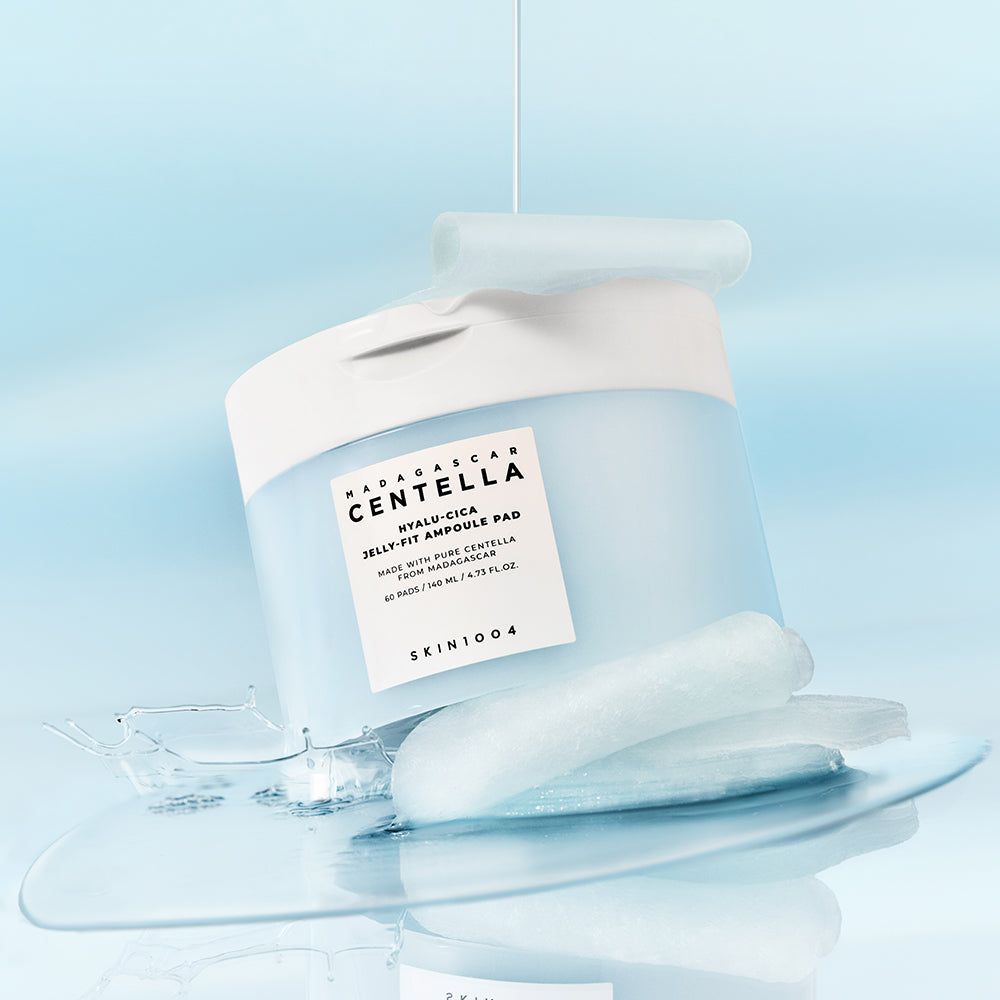 Blau-weißer Behälter, Flüssigkeit fließt heraus. Pads und Flüssigkeit auf Oberfläche. Text: CENTELLA, HYALU-CICA JELLY-FIT AMPULE PAD, SKIN1004.