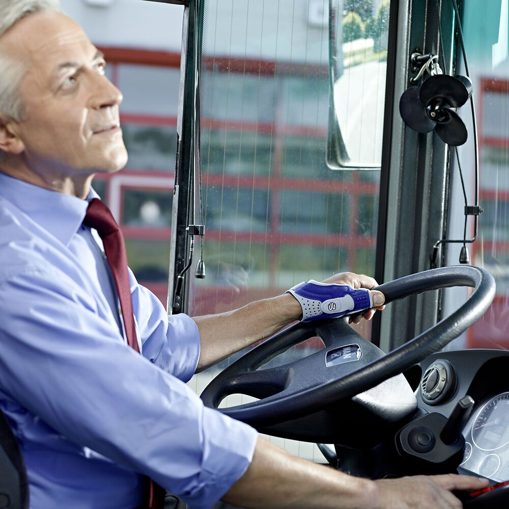 Mann am Steuer eines Busses, trägt Handgelenkbandage. Nahaufnahme.