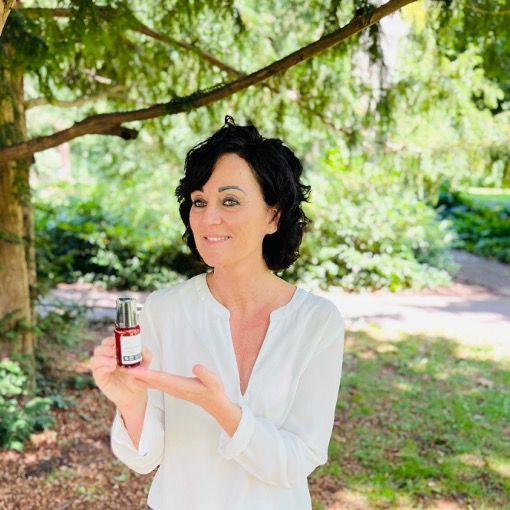Frau hält Produktflasche. Produkt: oxy8 Hydrating Face Cream. Hintergrund: Bäume und Grün.