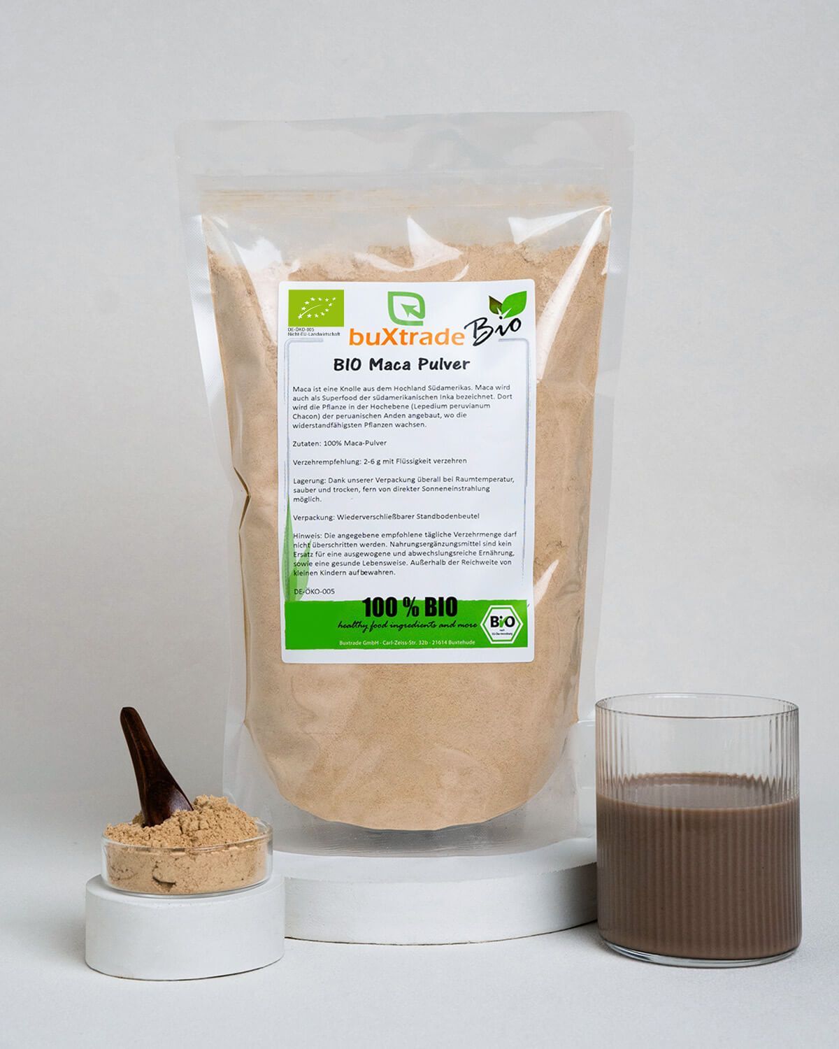 Buxtrade Bio Maca Pulver Beutel neben einem Glas mit braunem Getränk und einem Löffel mit Pulver.