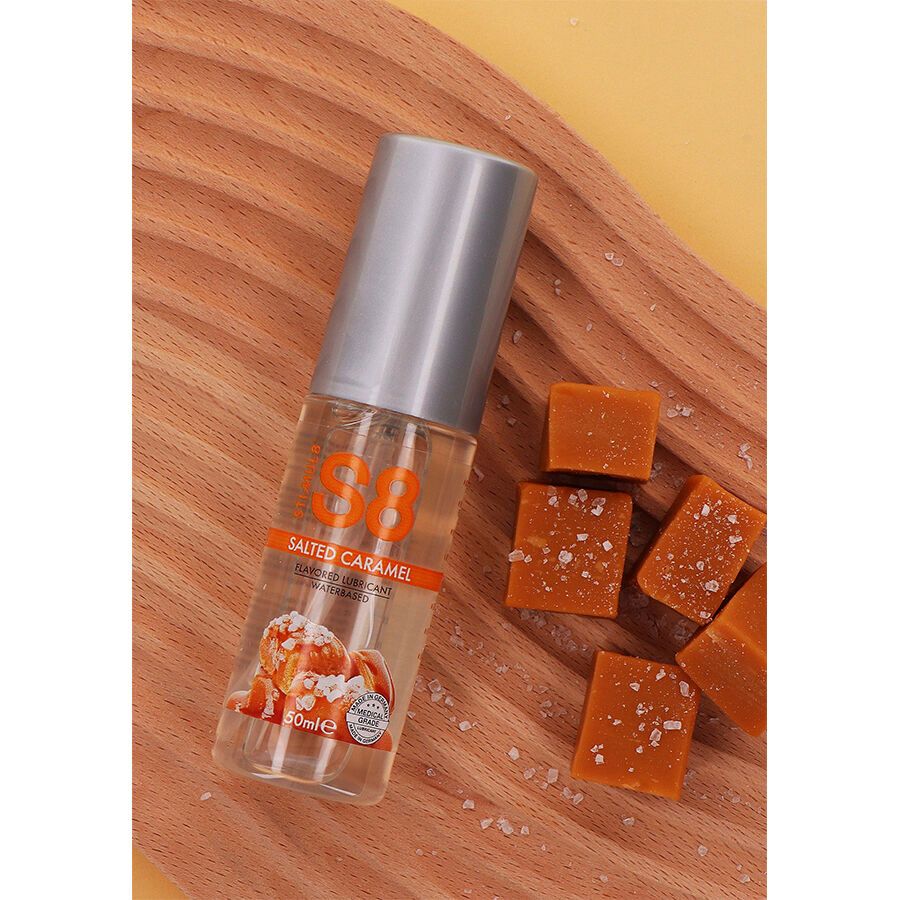 Flasche mit silbernem Deckel, auf Holzbrett. Orangefarbener Aufdruck: S8, Salted Caramel, Wasserbasiert. Karamellbonbons daneben.