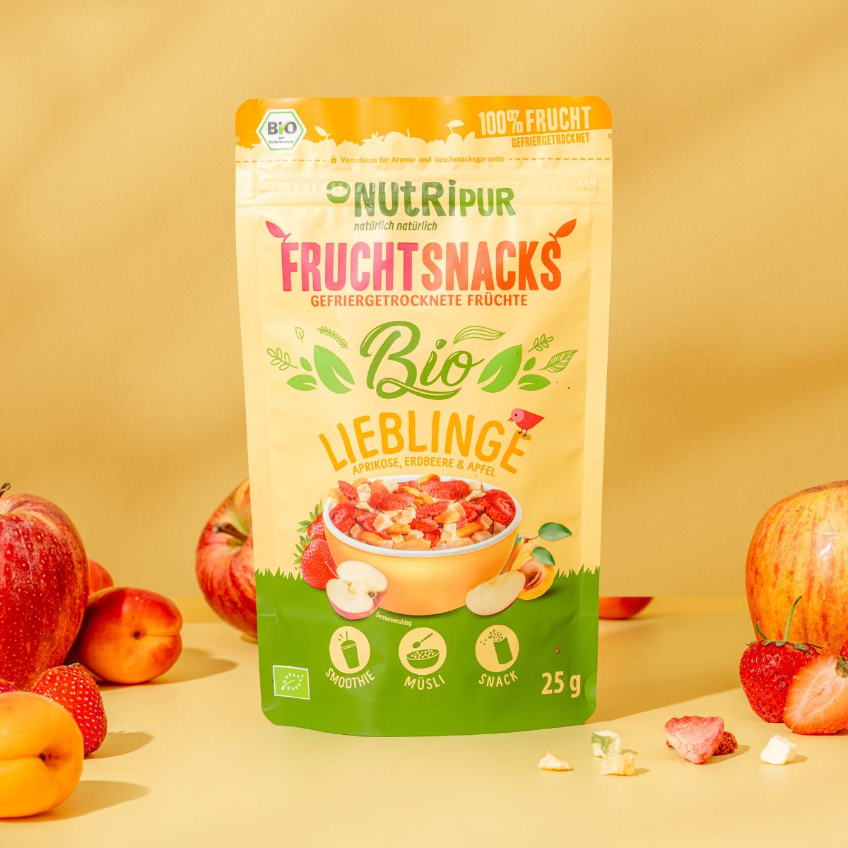 Beutel mit gefriergetrockneten Früchten. Aufschrift: NutriPur, Frucht Snacks, Bio Lieblinge. Bio-Siegel. 25g. Äpfel, Erdbeeren und Aprikosen daneben.