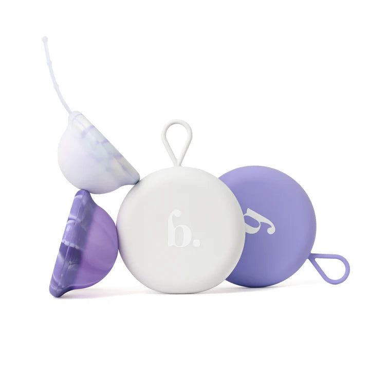 Verschiedene Menstruationsscheiben in Lila und Weiß. Eine Scheibe ist geöffnet, mit Rückholband. Runde Behälter mit Logo.