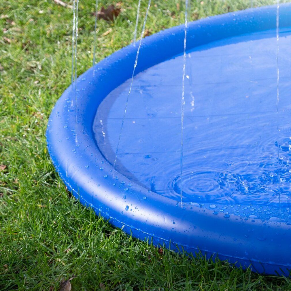 Nahaufnahme eines blauen, runden Pools mit Wasserstrahlen. Der Pool steht auf einer grünen Wiese. Wasser spritzt in die Luft.