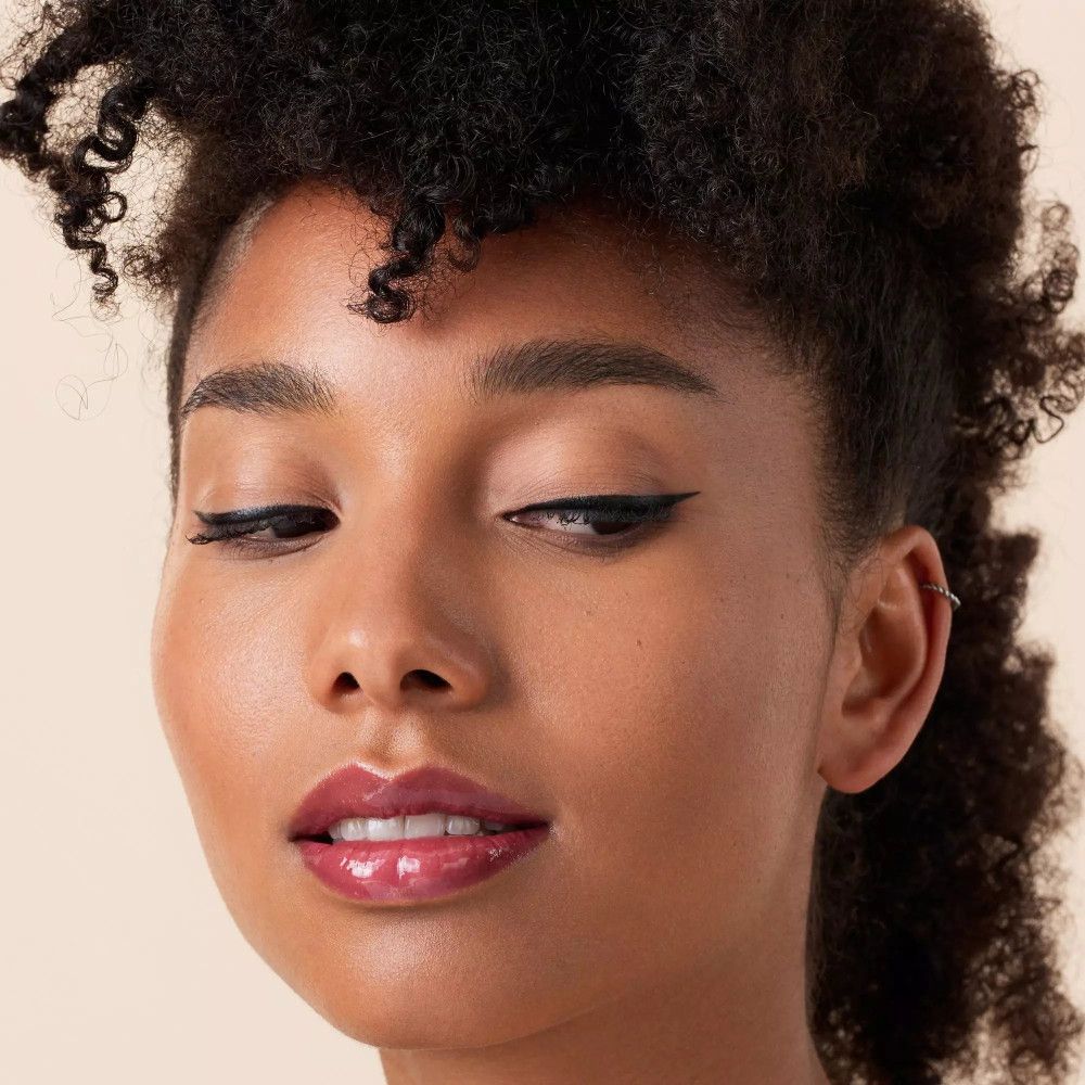 Nahaufnahme eines Gesichts mit Make-up. Schwarzer Eyeliner, glänzende Lippen. Dunkle Haut.