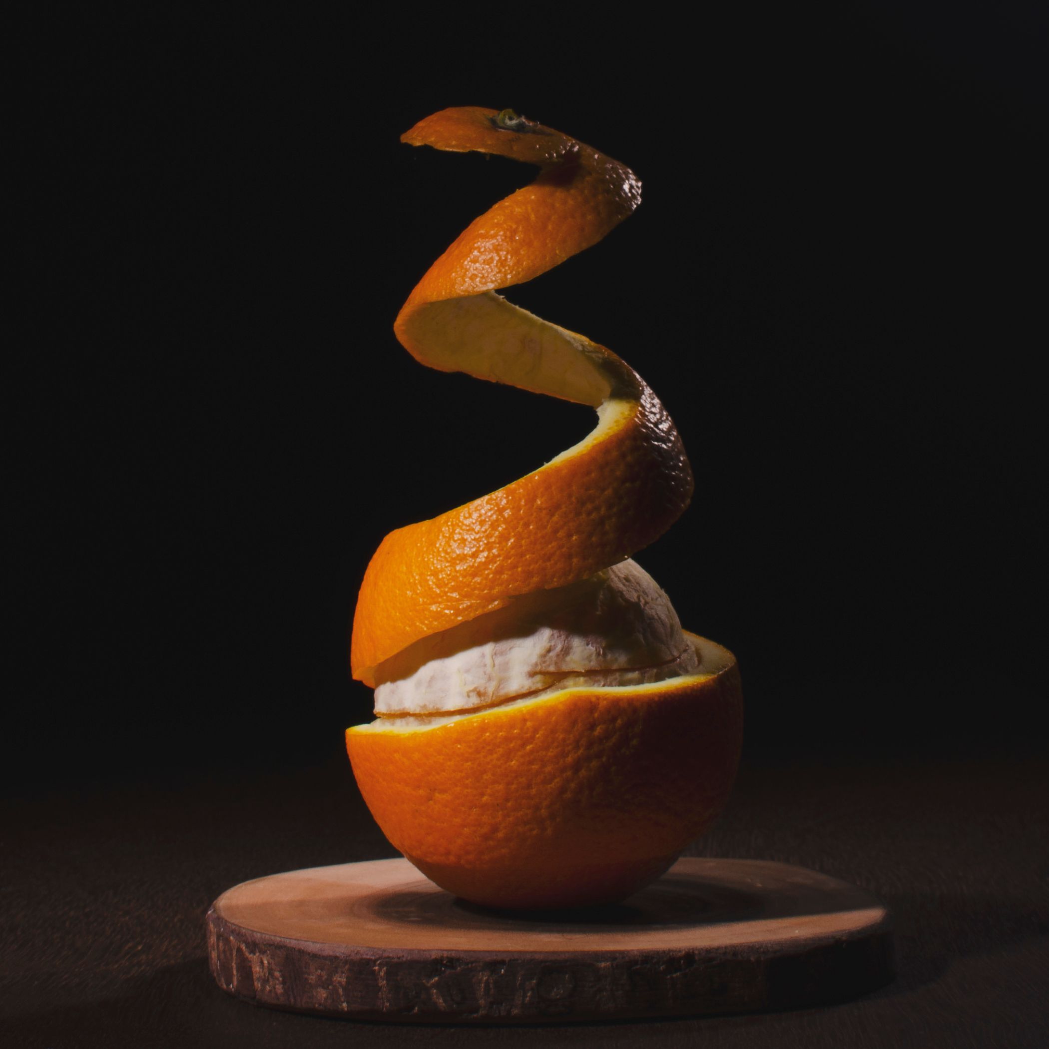 Halbe Orange mit spiralförmig geschälter Schale, auf Holzbrett. Dunkler Hintergrund. Natürliche Beleuchtung.