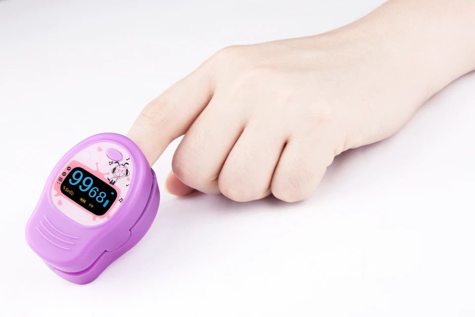 Fingerpulsoximeter am Finger. Lila Gerät mit Display. Zeigt SpO2- und PR-Werte an.