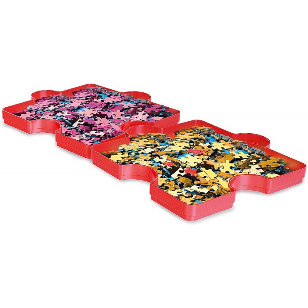 Zwei rote Puzzleteile-Tabletts, gefüllt mit Puzzleteilen in verschiedenen Farben. Blick von oben, leicht schräg.