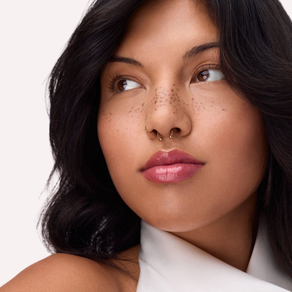 Porträt einer Frau mit dunklen Haaren und Sommersprossen. Sie trägt rosa Lipgloss. Blick zur Seite.