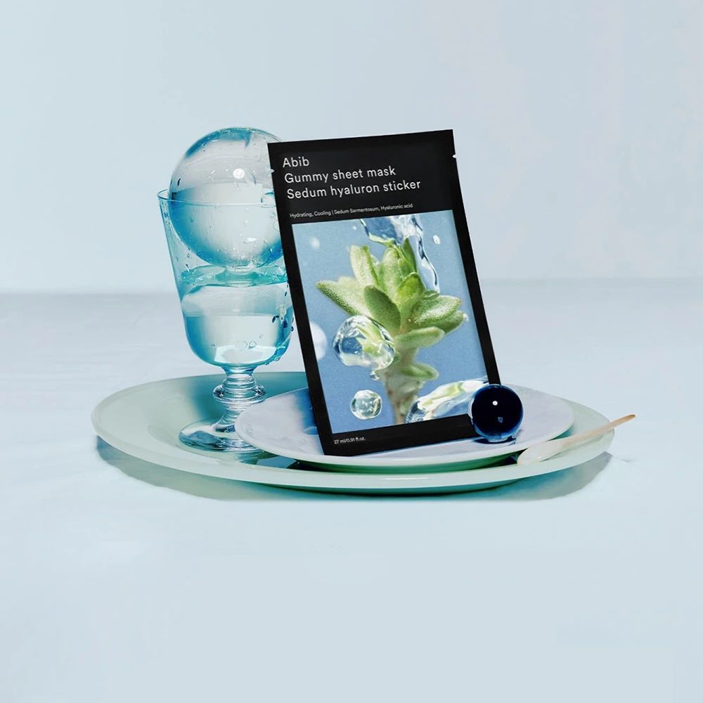 Abib Gummy Sheet Mask Sedum Hyaluron Sticker auf einem Teller mit Glas und Wasser.
