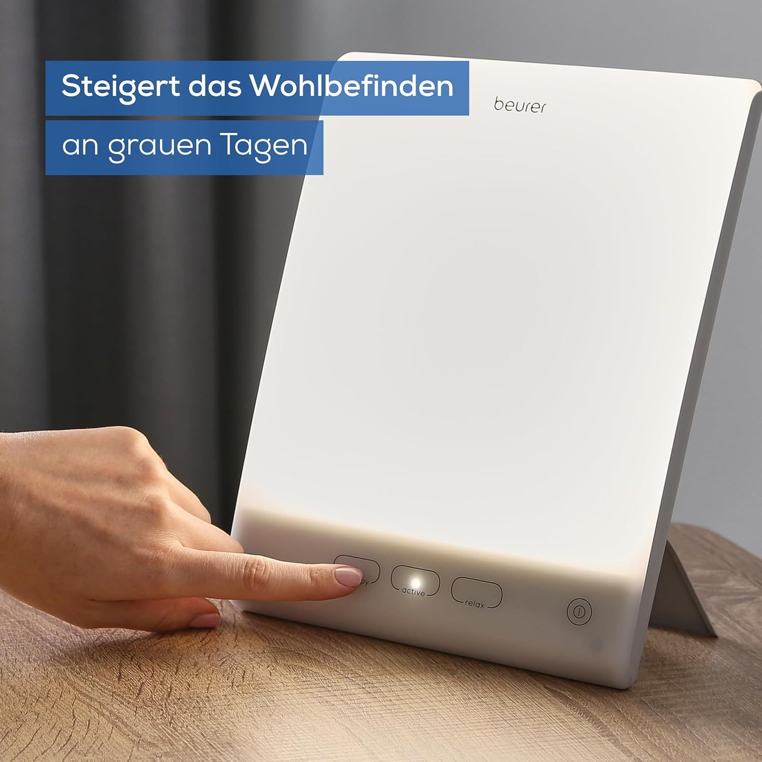 Tageslichtlampe. Eine Hand berührt die Bedienknöpfe. Text: Steigert das Wohlbefinden an grauen Tagen.