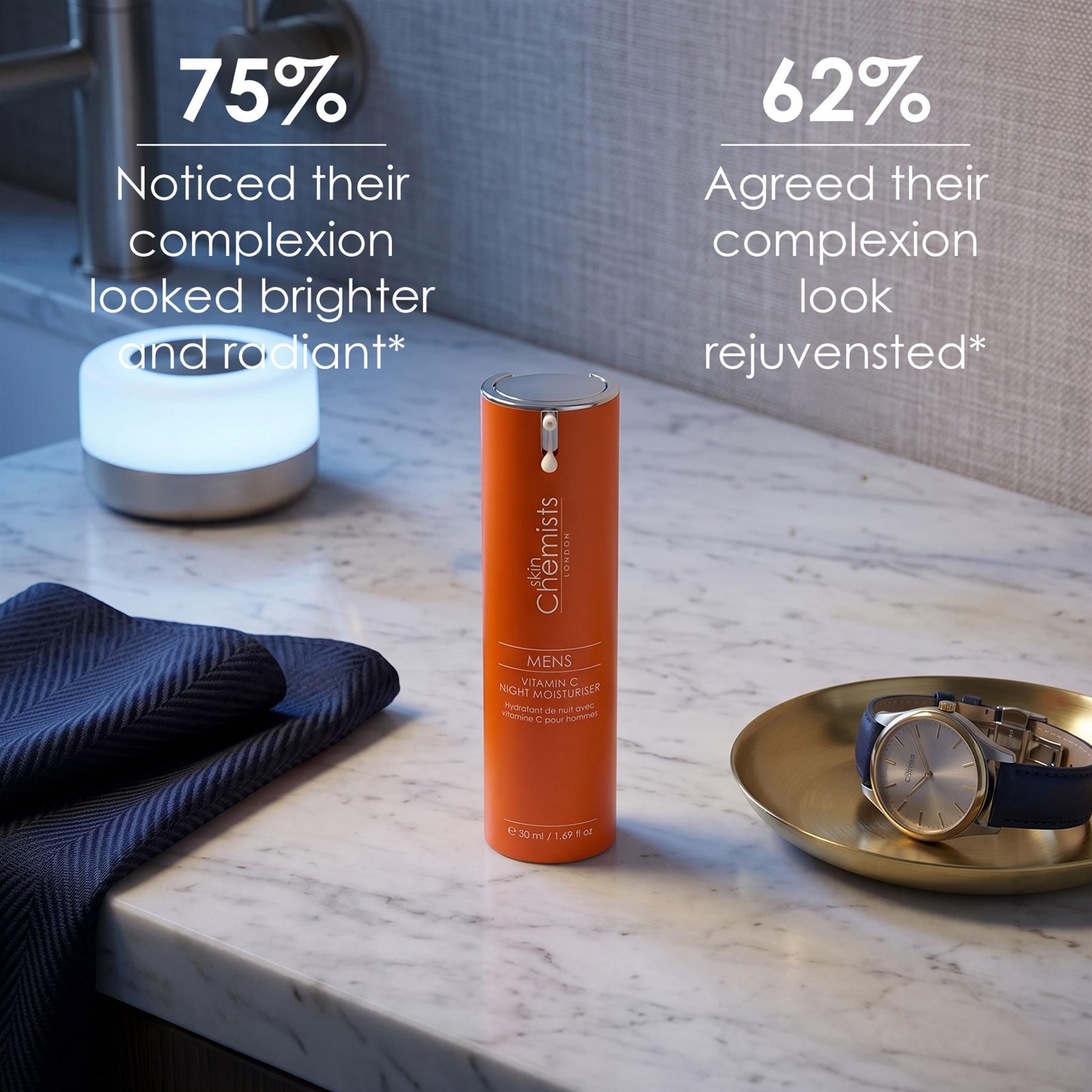 Orangefarbene Flasche SkinChemists Vitamin C Nacht-Feuchtigkeitscreme auf einem Marmortisch neben einem Handtuch und einer Uhr.