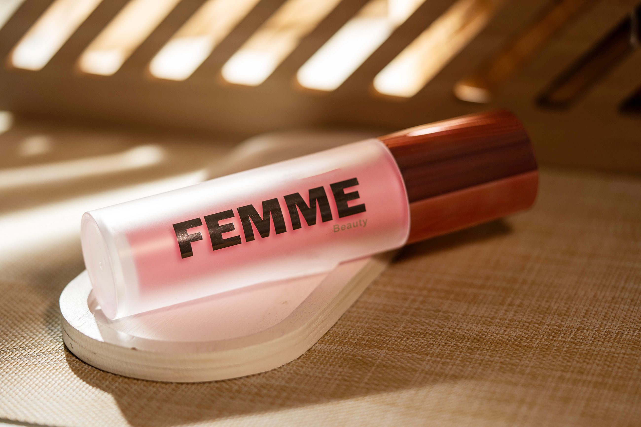 Liegende Flasche mit mattem Finish und rosafarbenem Inhalt, roségoldfarbener Verschluss. Marke: FEMME Beauty.