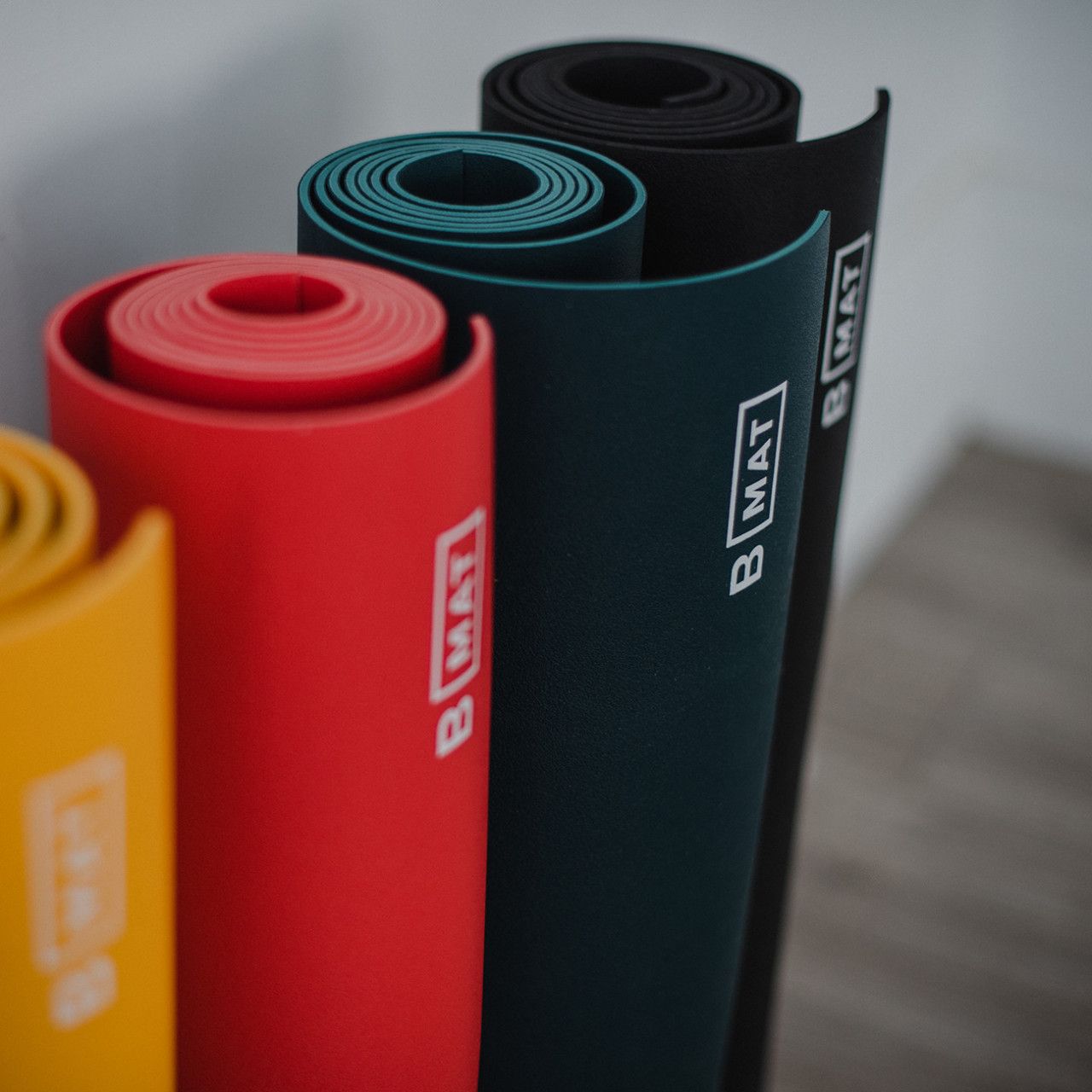 Gerollte Yogamatten in verschiedenen Farben, darunter Ocean Green. Logo B MAT.