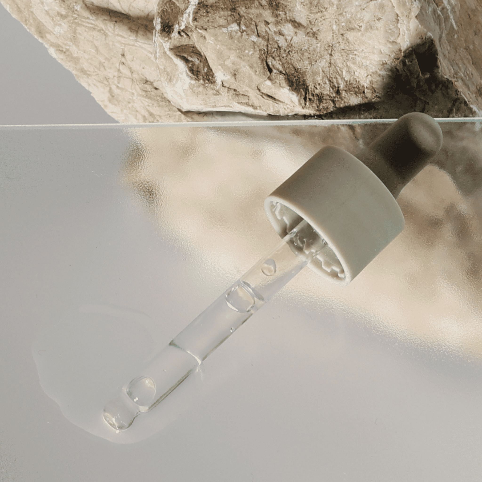 Pipette mit grauem Aufsatz und klarem Serum auf spiegelnder Oberfläche.
