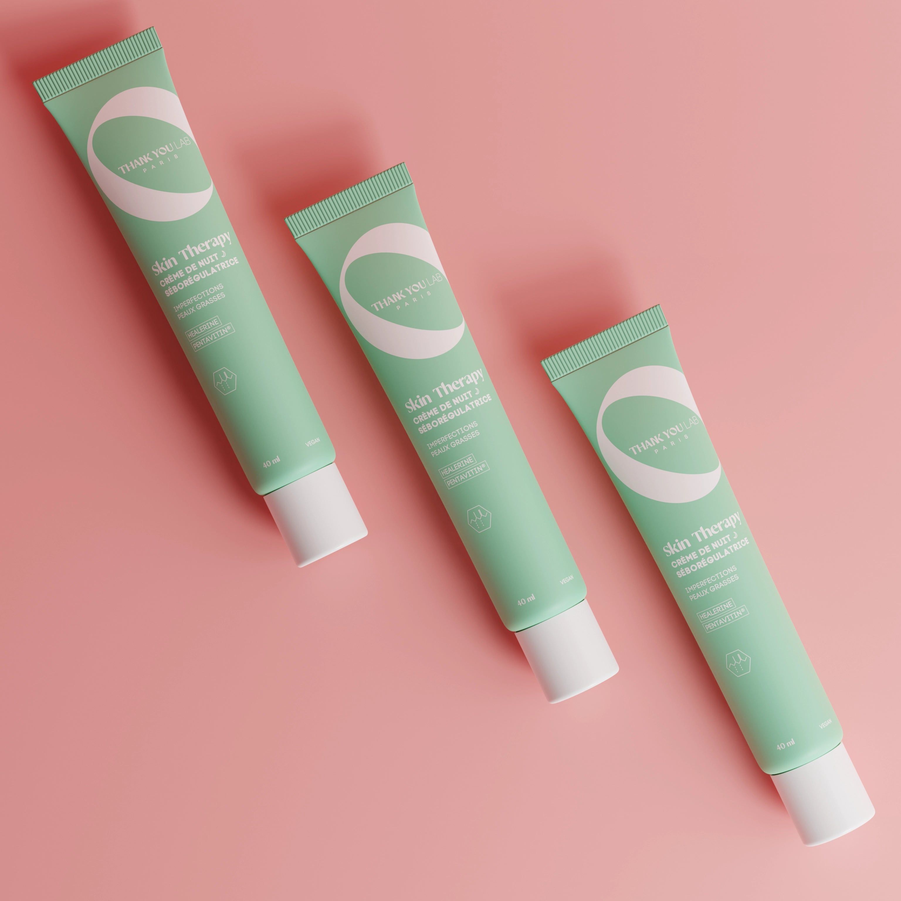 Drei grüne Tuben auf rosa Hintergrund. Aufschrift: Skin Therapy, Crema notte. Weiße Kappe.